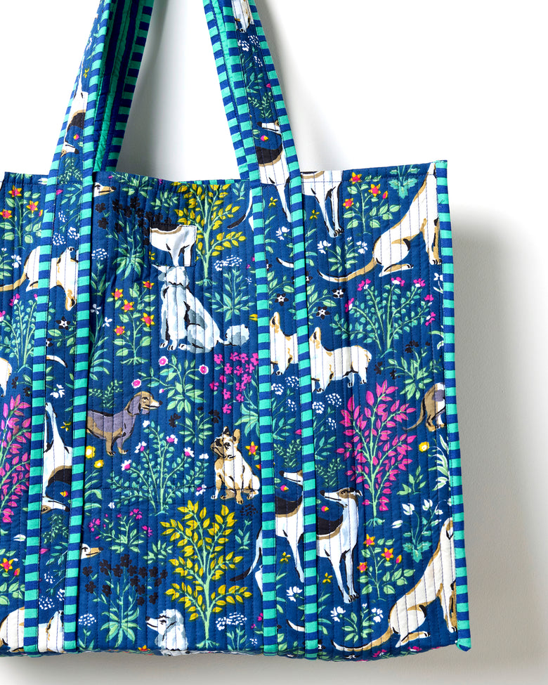 Close view of the indigo quilted traveler tote showing dog-and-flower print panels, striped handles, and a front pocket.