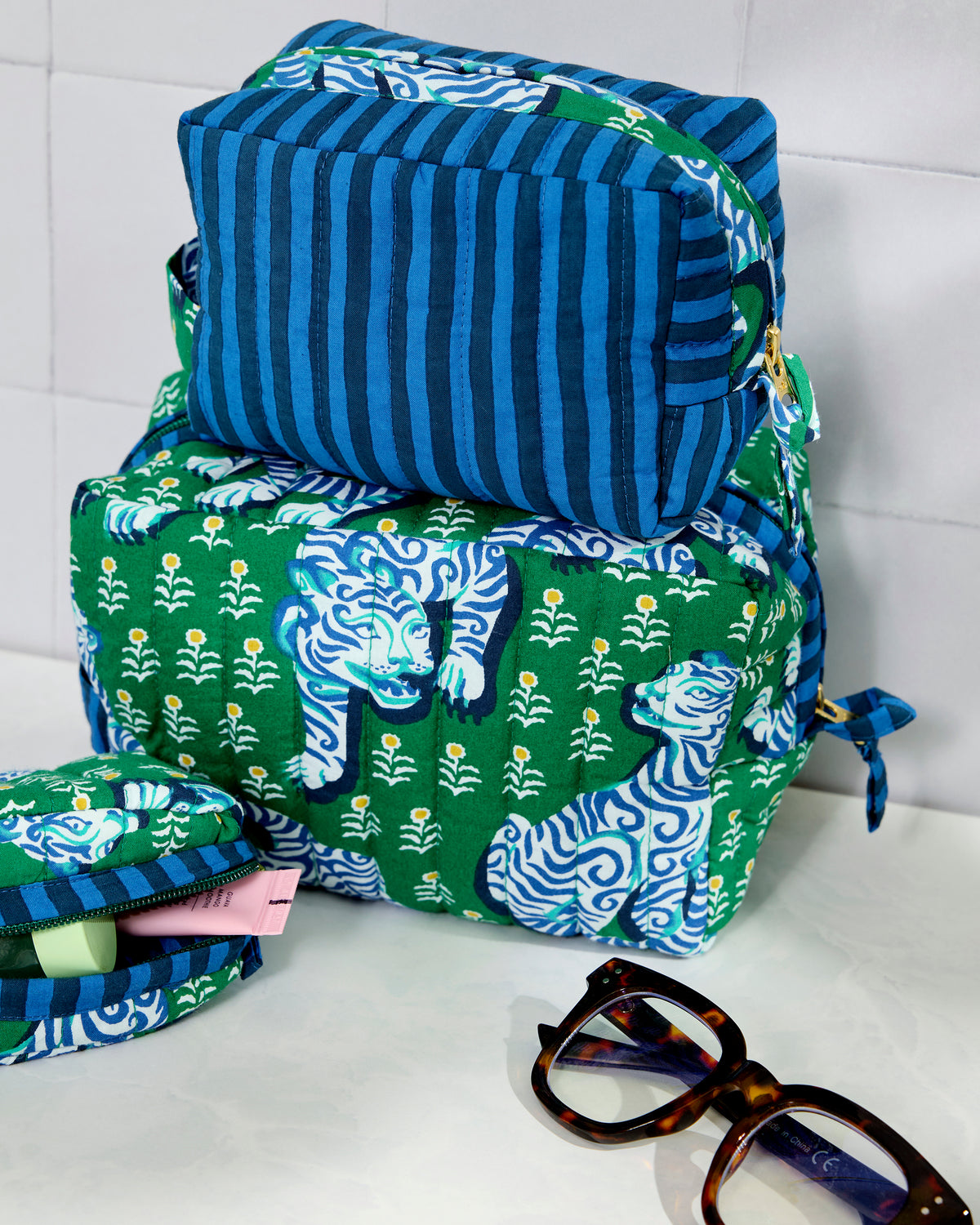 Three quilted pouches in jade and blue, stacked together; the large and small pouches have a tiger print and the medium pouch has blue stripes.