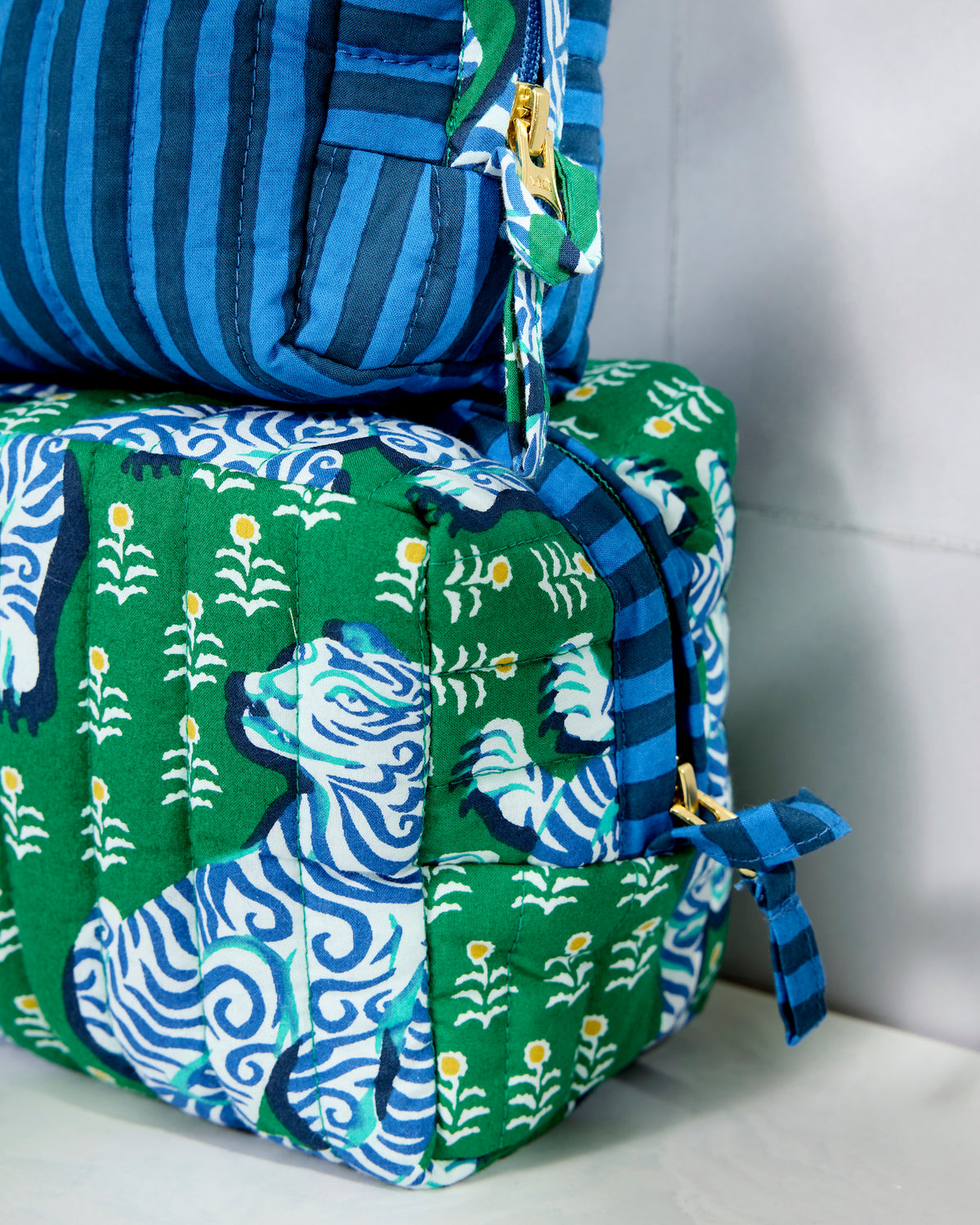 Close-up of the striped medium pouch beside the tiger-print large pouch, showing quilted stitching, zippers, and fabric ties.