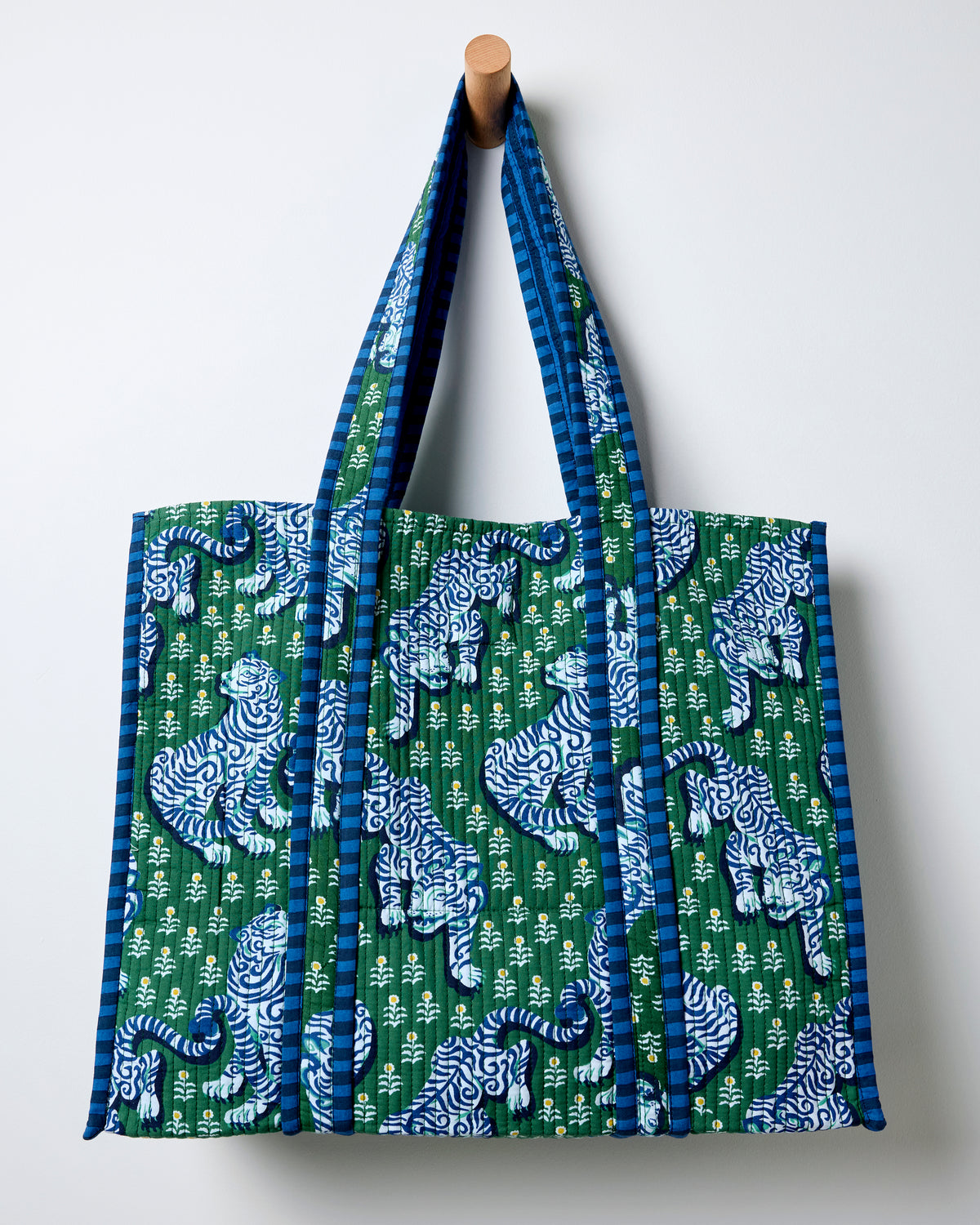 Quilted jade tote hanging from a wall peg, with blue-and-white tigers, small white flowers, and blue striped handles and edging.