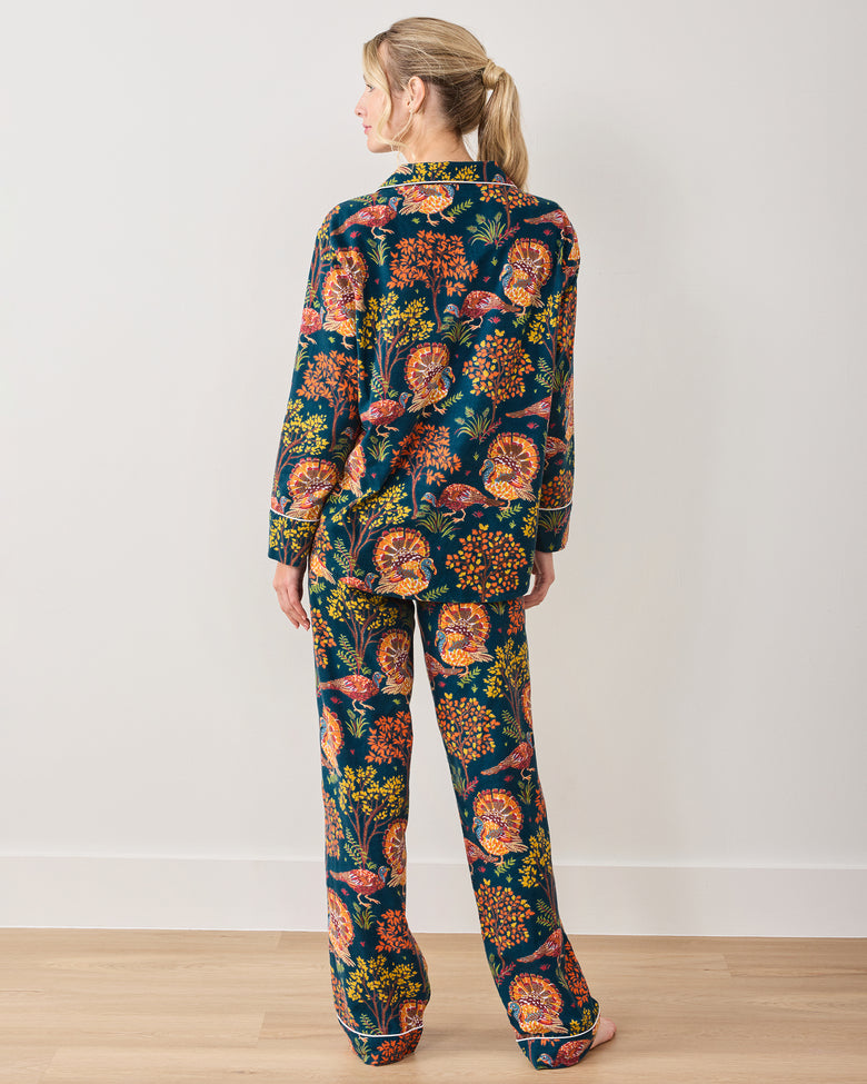 Back view of a model wearing the Turkey Trot navy long-sleeve pajama set with an autumn turkey and foliage print.