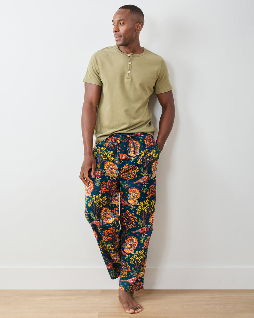Front view of the navy Turkey Trot long pajama pants with colorful turkey and autumn foliage print, styled with a plain short-sleeve shirt.