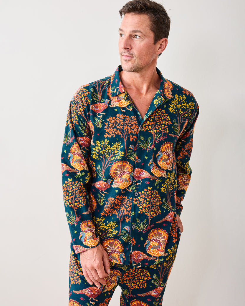 Front three-quarter view of a model wearing the navy Turkey Trot long pajama shirt and pants, printed with colorful turkeys and autumn foliage.