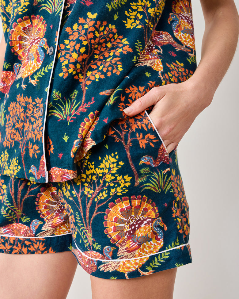 Close view of the navy Turkey Trot short pajama shorts and top showing the side pocket, white piping, buttons, and colorful turkey and autumn foliage print.