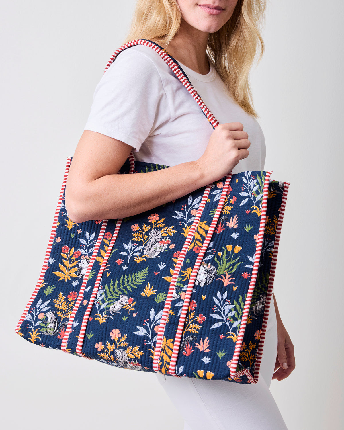 Indigo Woodland Critters traveler tote carried over a shoulder, showing its quilted woodland print and striped trim.