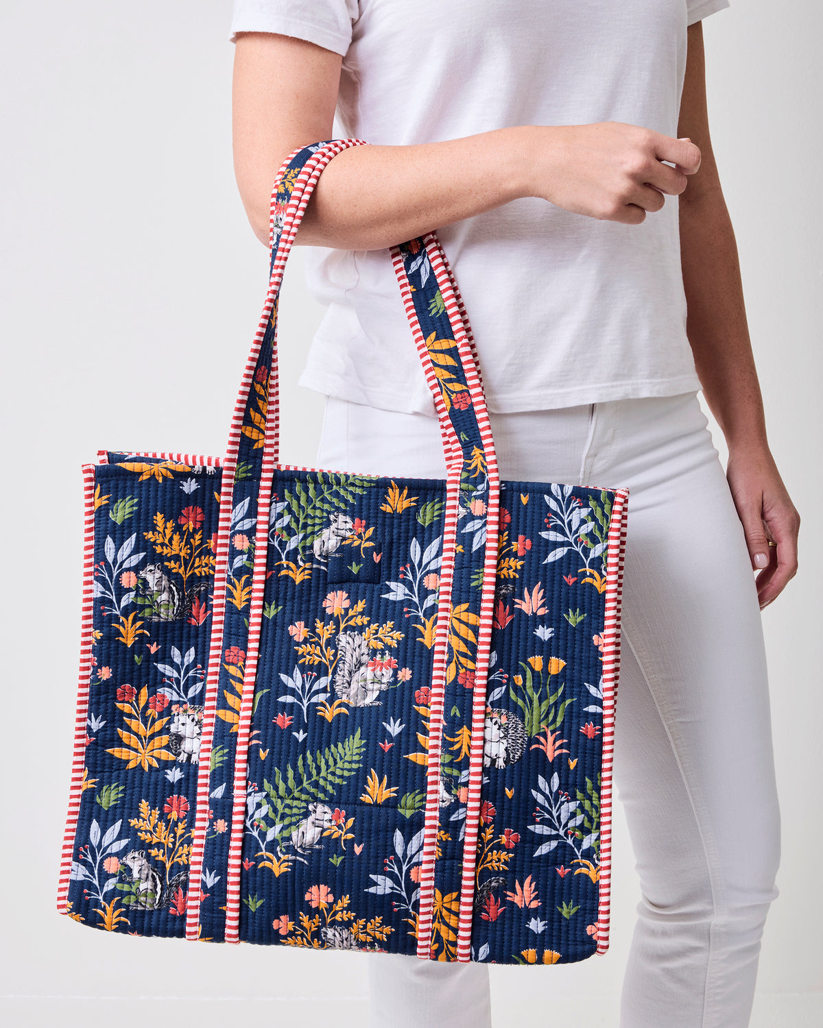 Front view of the indigo Woodland Critters traveler tote with long straps, quilted woodland print, and striped trim.