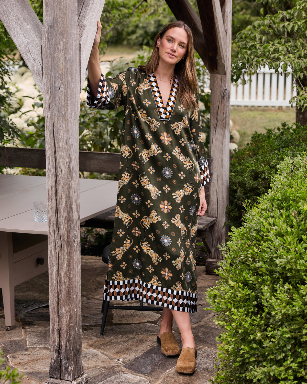 Person wearing an olive caftan with a repeating leopard-and-flower print and geometric trim at the neckline, cuffs, and hem.