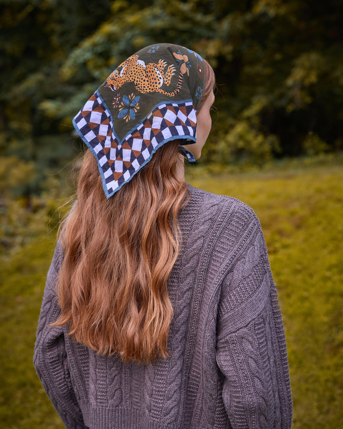 Back view of a printed bandana scarf worn over the head, featuring leopard, floral, and geometric motifs.