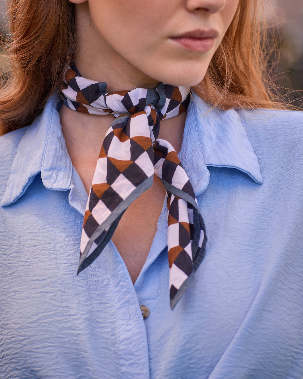 Printed bandana scarf knotted around the neck, showing its geometric pattern and pointed ends.