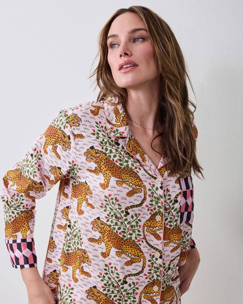 Close-up of a model wearing the Bagheera blush pajama top with leopard, jungle cat, foliage, and floral print, contrasting checkered cuffs and a chest pocket.