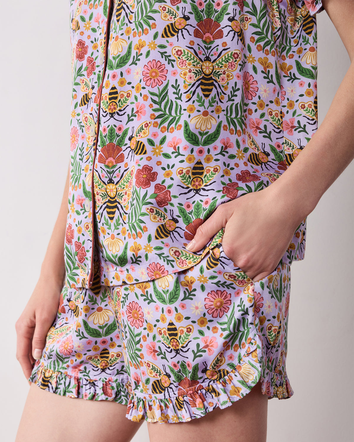 Close-up of the lavender Bee Tapestry pajama set showing the printed top, pocket, and ruffled shorts hem.