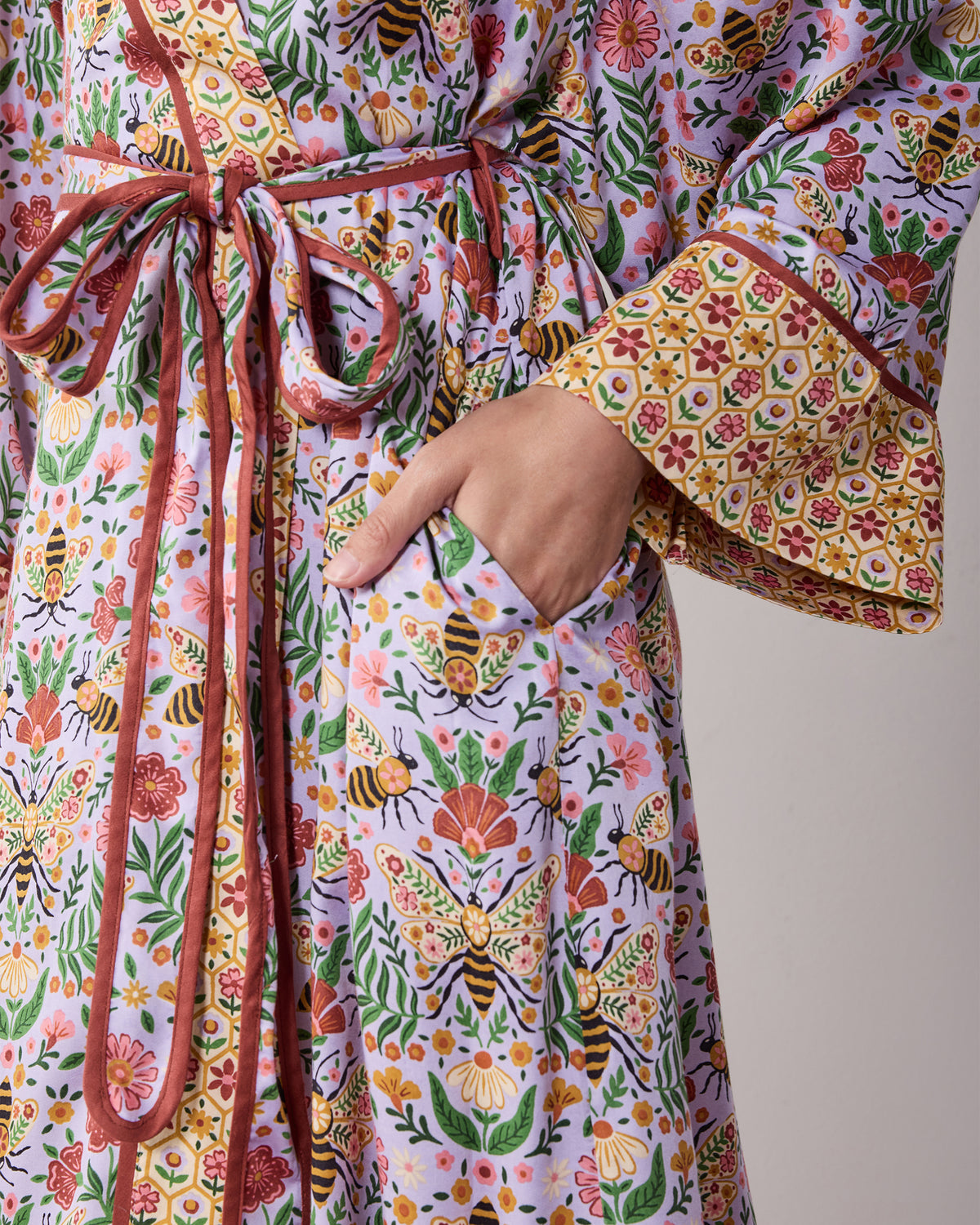 Close-up of the lavender Bee Tapestry robe showing the floral bee print, tie belt, pocket, and contrasting cuff.