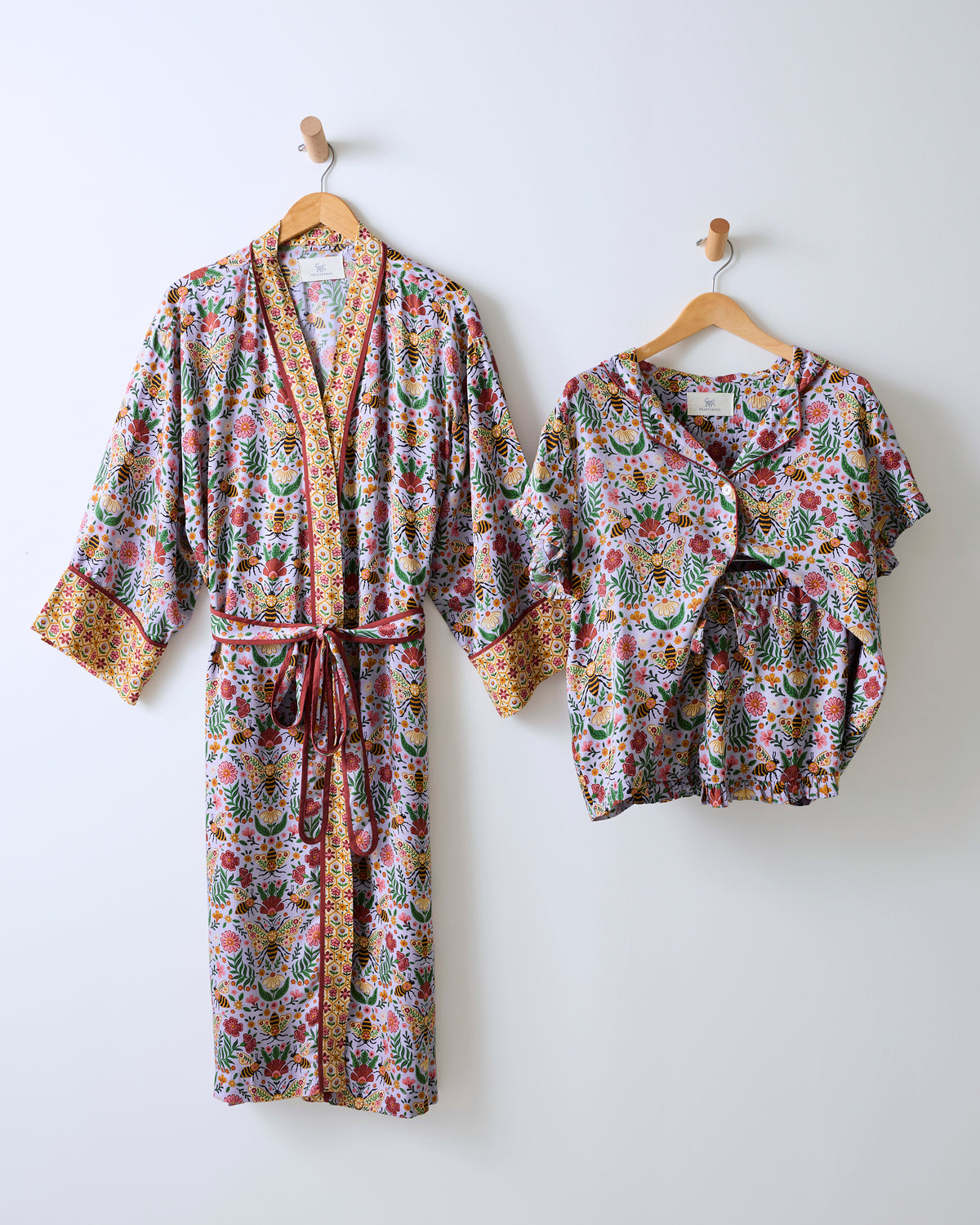 White floral-and-bee print robe with belt beside a matching short-sleeve ruffle pajama set.