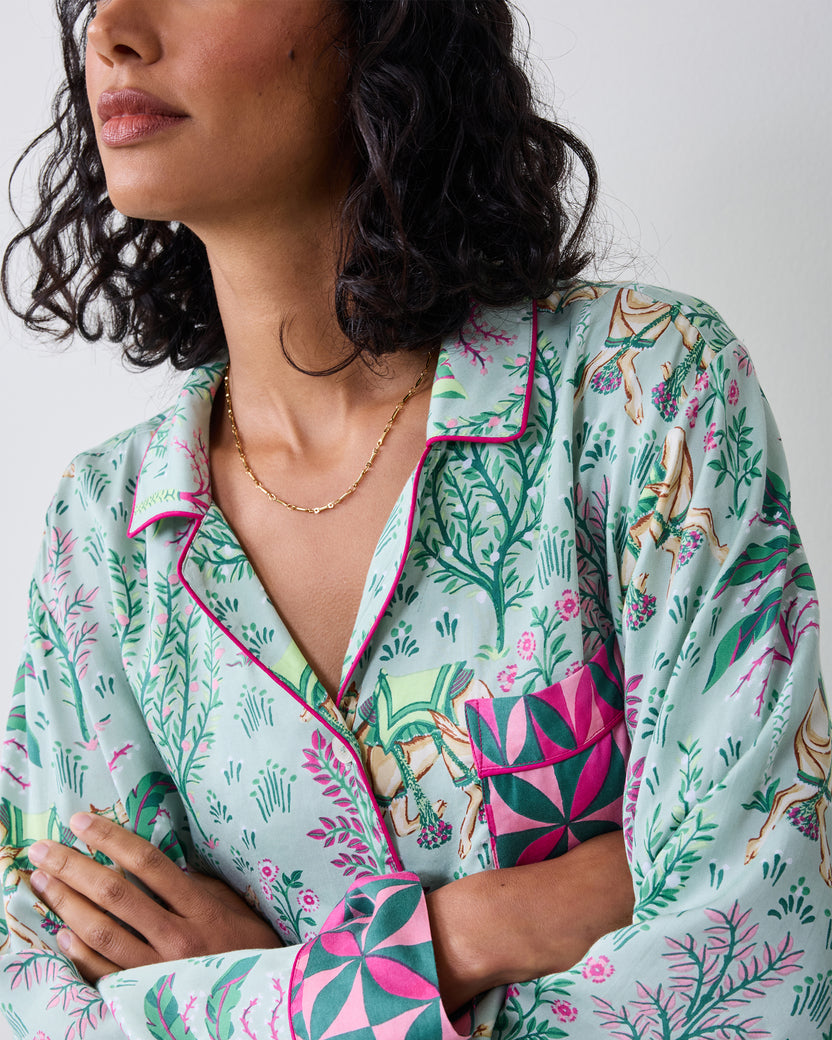 Close-up of the avocado Camel's Courtyard pajama top showing the open collar, camel-and-botanical print, contrasting geometric chest pocket, and cuff.
