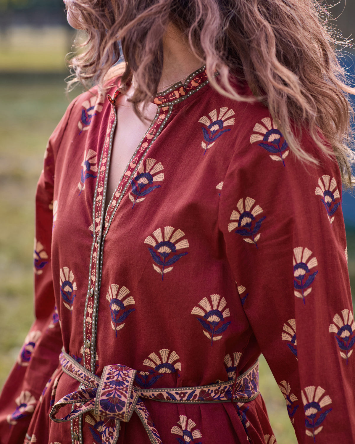 Close-up of the Maybelle dress showing the red floral print, button-front placket, decorative trim, and tied waist belt.