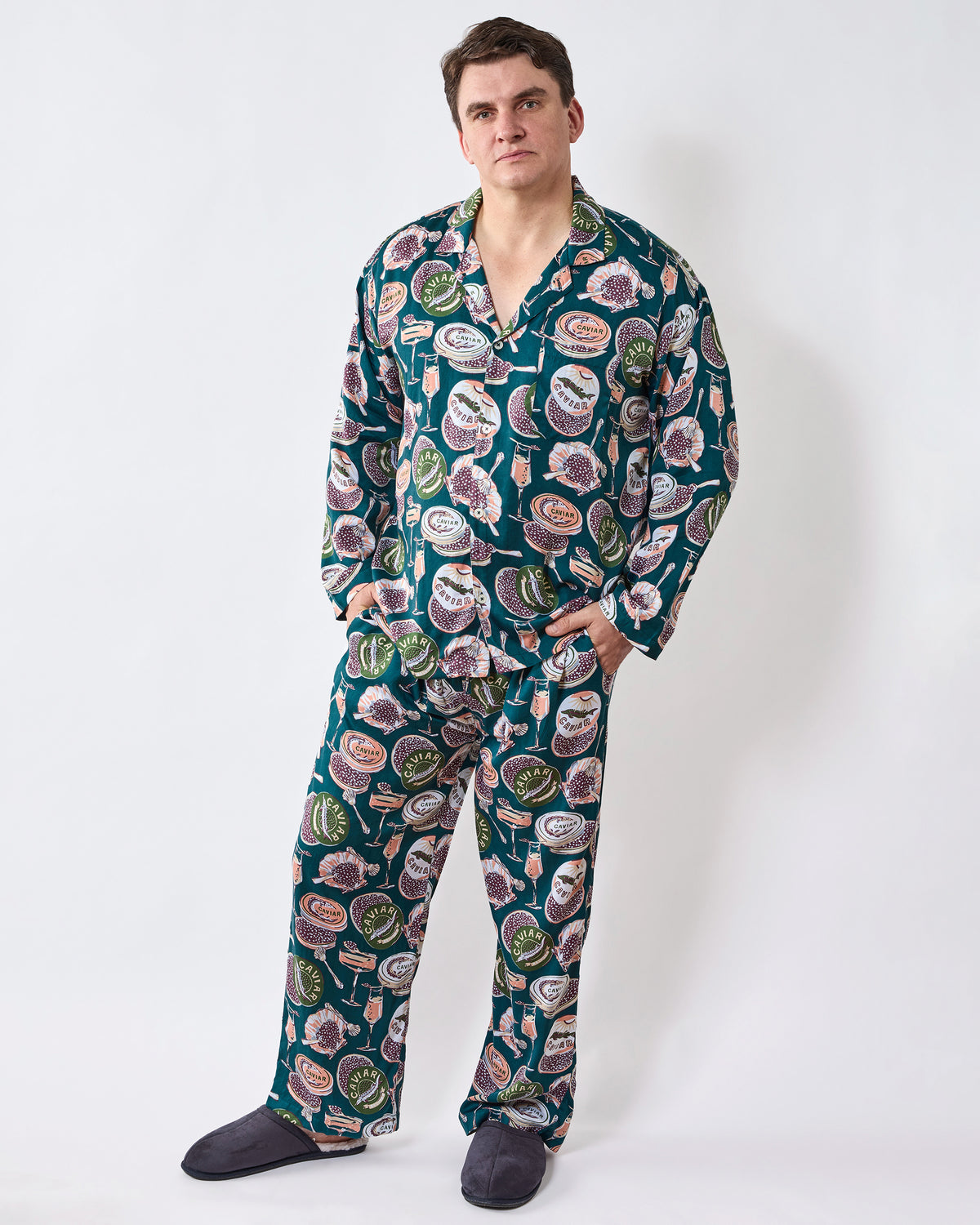 Person wearing a long dark teal pajama set with a collared button-front top and matching full-length pants, printed with caviar and champagne motifs.