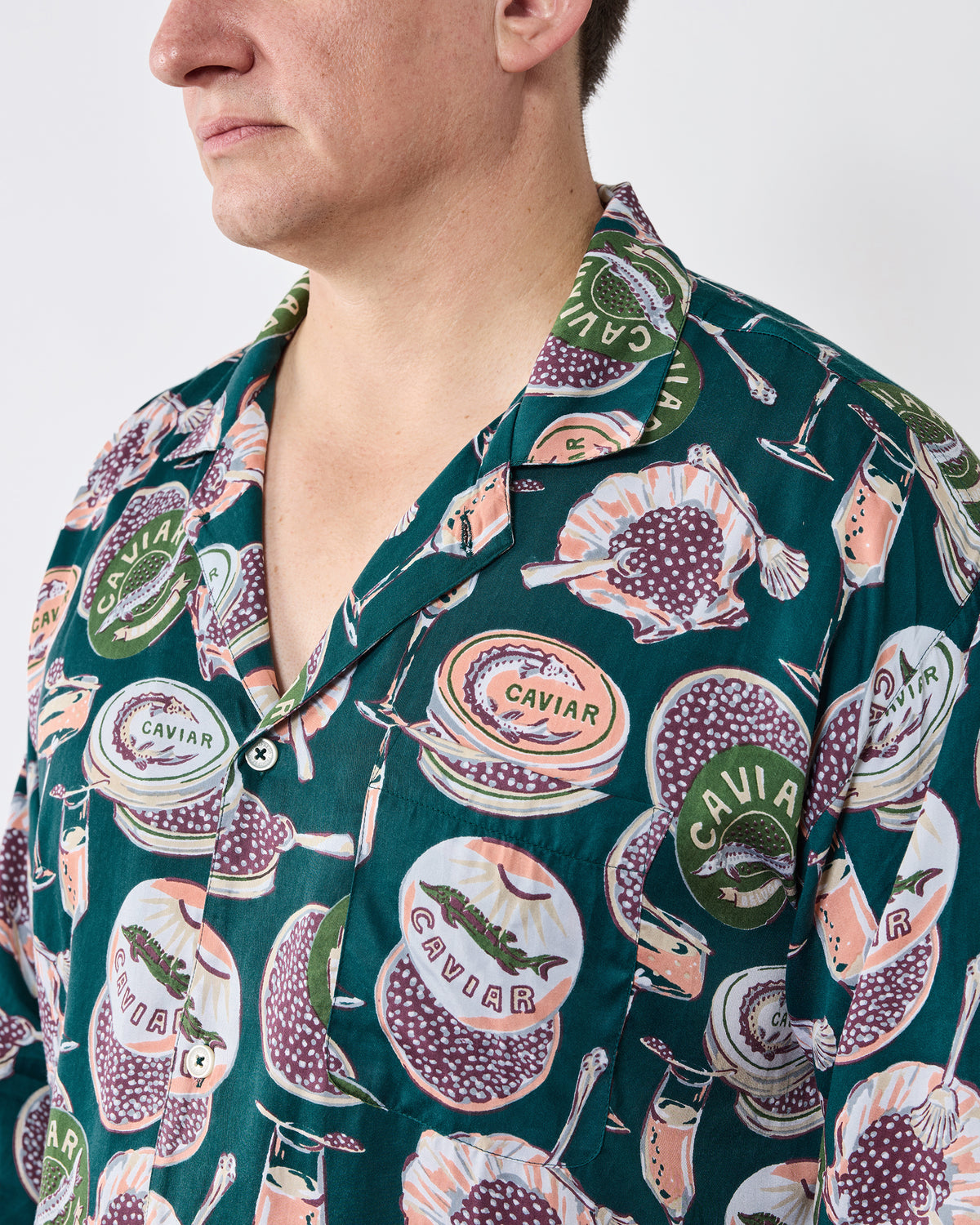 Close view of the long pajama top showing its notched collar, buttons, chest pocket, and caviar-and-champagne print.