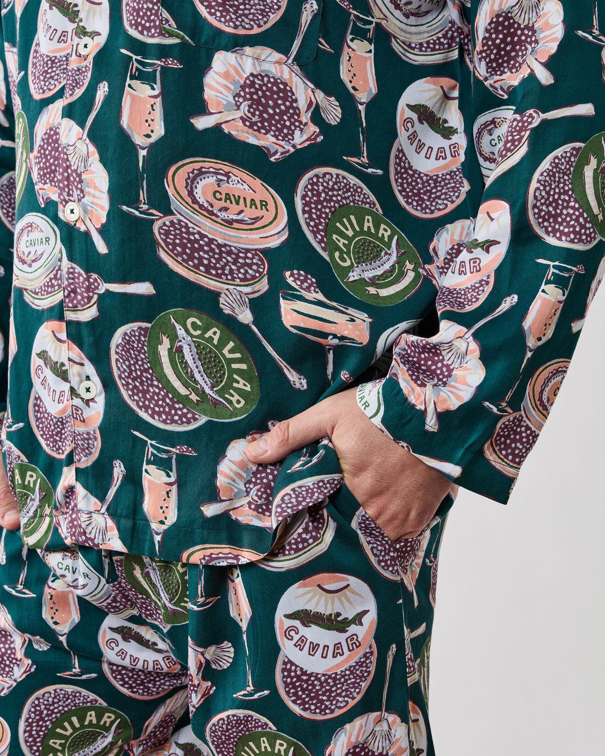 Close view of the long pajama top and pants showing the button front, sleeve cuff, side pocket, and caviar-and-champagne print.