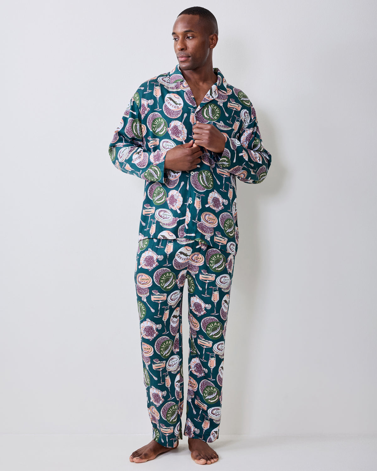 Front view of a person wearing a long-sleeve button-front pajama top and matching full-length pants with a caviar-and-champagne print.
