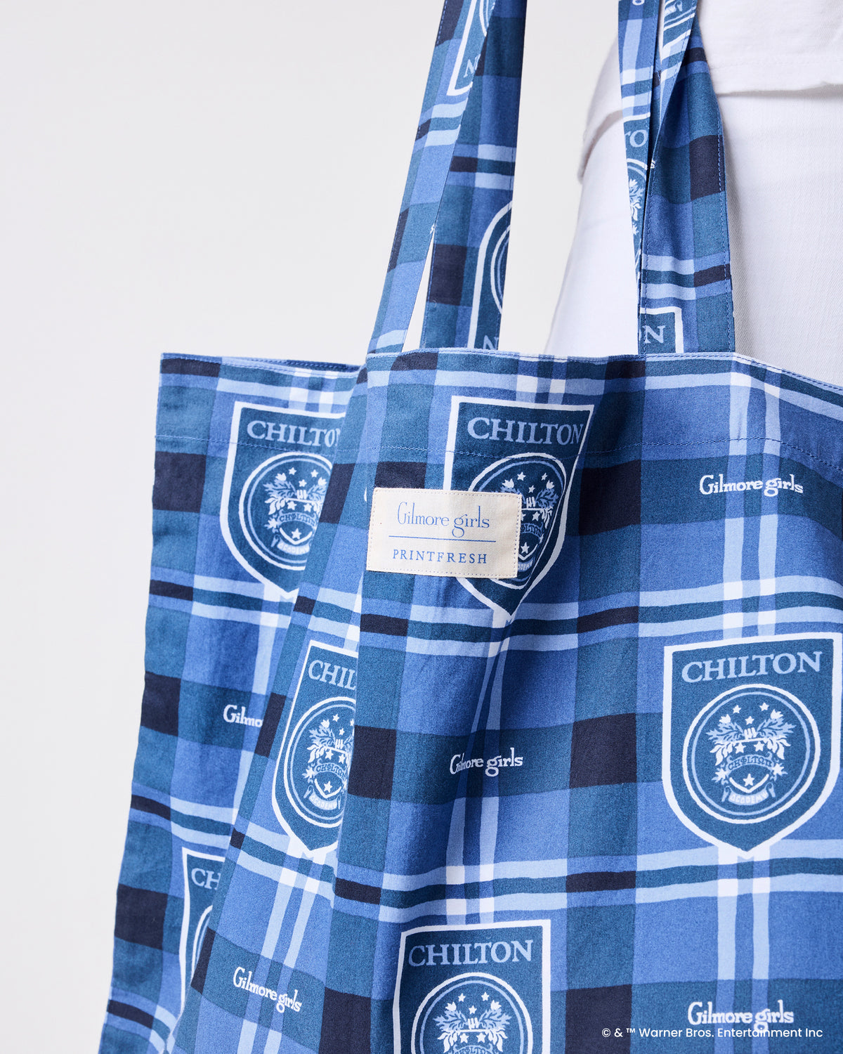 Angled close-up of the blue plaid tote bag showing repeated Chilton crest and Gilmore Girls prints and the sewn label.