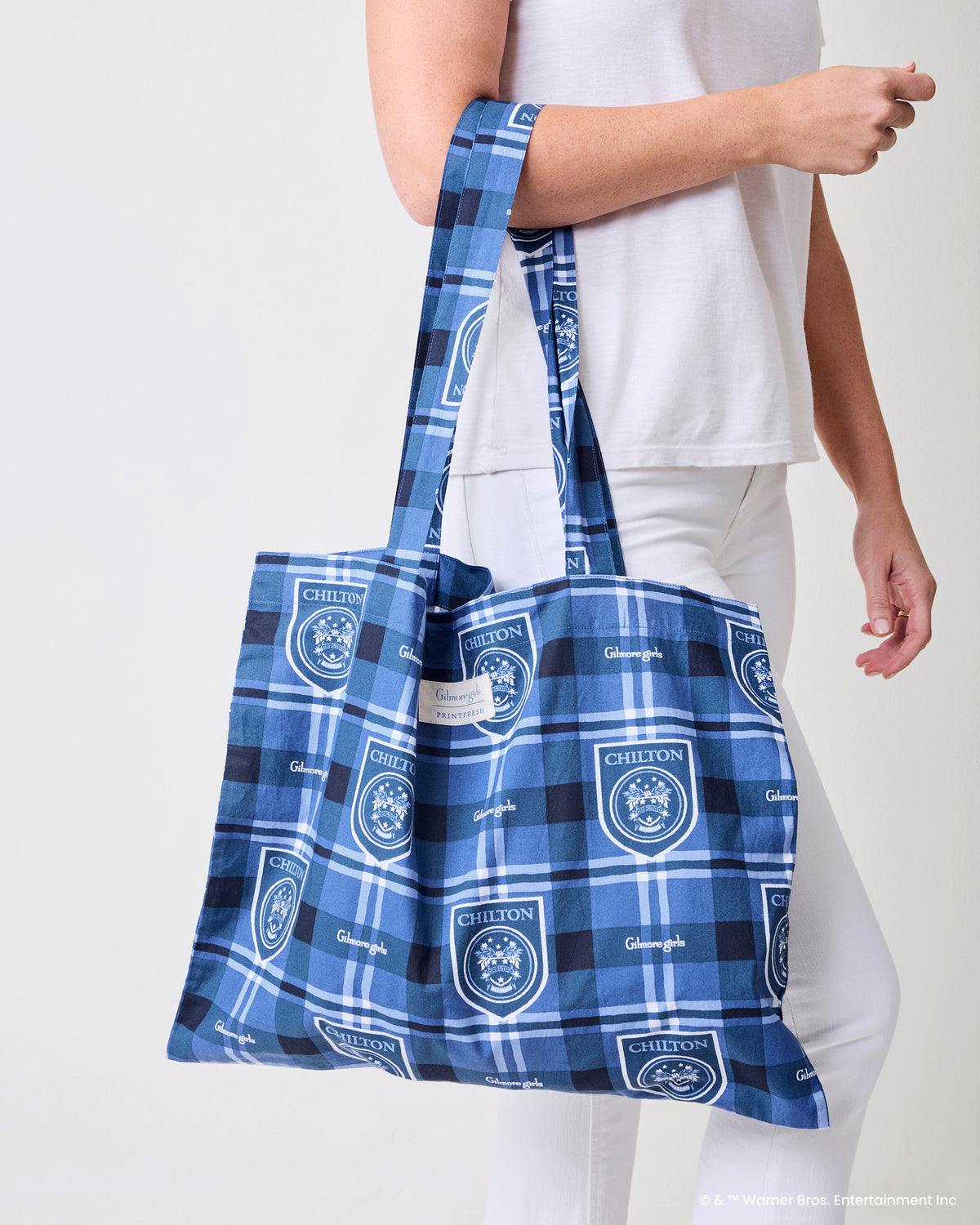 Person carrying the blue plaid Chilton crest and Gilmore Girls print tote by its long handles.