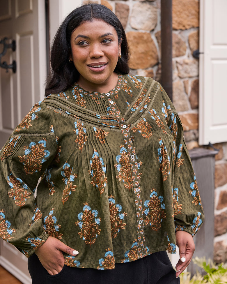 Close front view of the deep olive Belmont blouse showing its blue and brown floral print, pleated details, lace-trimmed yoke, and white buttons.