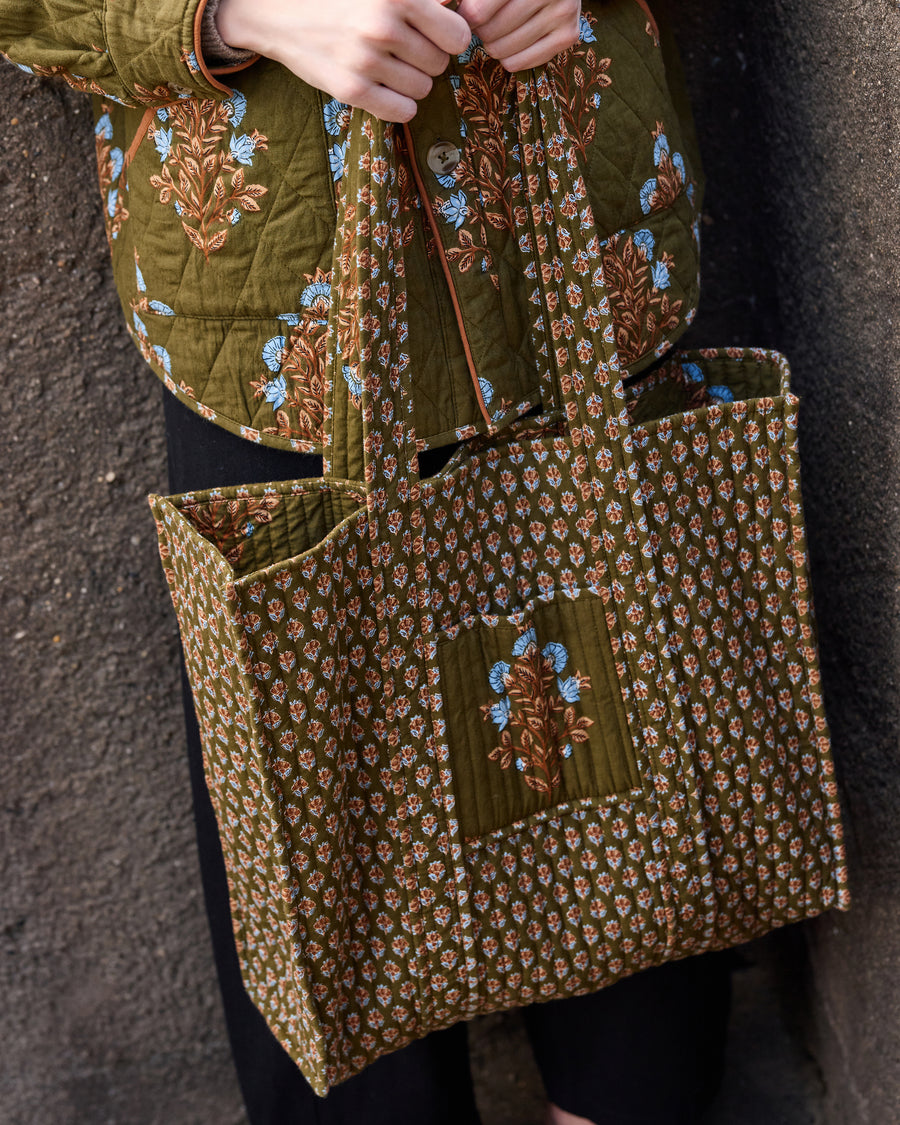 Close-up of the deep olive Traveler Tote showing its quilted floral panels, contrasting patterned front pocket, and handles.