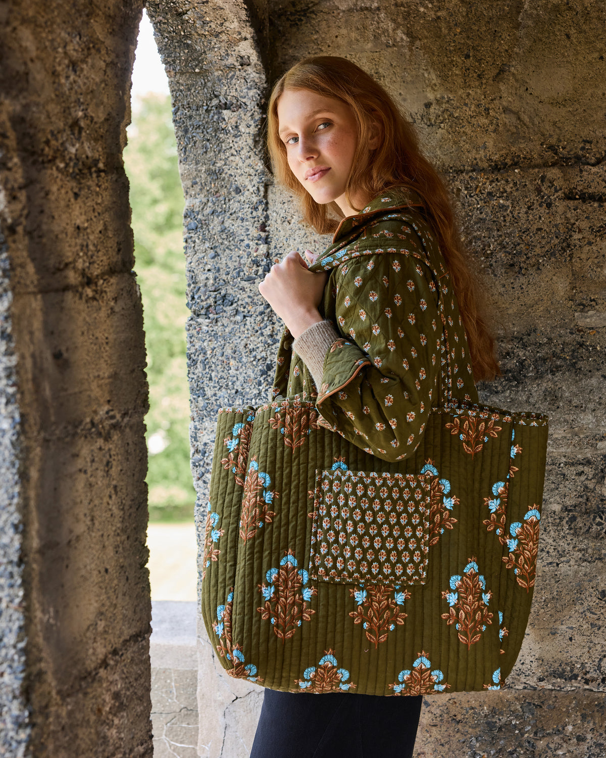 Side view of the deep olive quilted jacket and matching floral traveler tote, showing the tote’s front pocket and floral pattern.