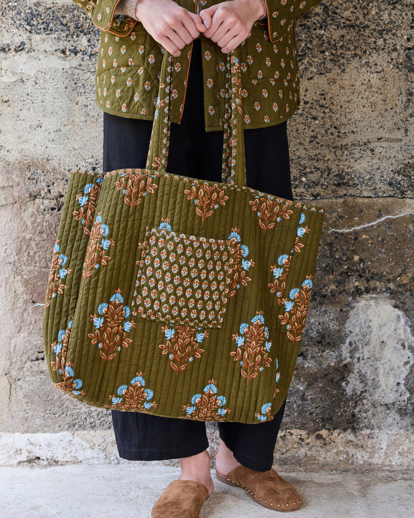 Front view of the deep olive Traveler Tote showing its quilted floral design, contrasting patterned pocket, and long handles.