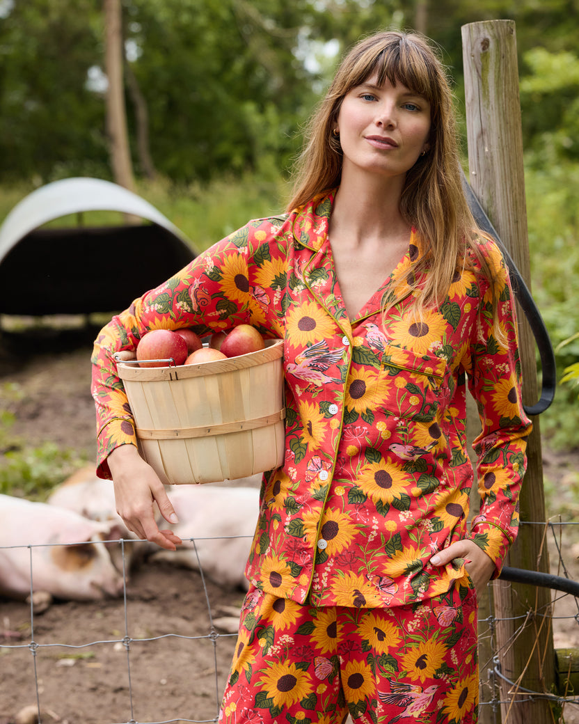 Model wearing the orange Autumn Sunflowers long pajama set and holding a basket of apples outdoors.
