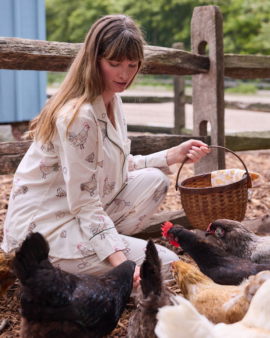 Side view of the buff Embroidered Hens pajama set, showing chicken illustrations while a person holds a woven basket among chickens.