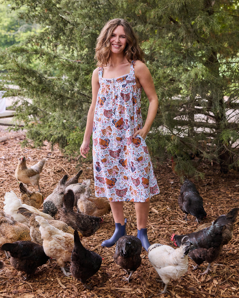 Person wearing a floral chicken-print sleeveless nightgown surrounded by chickens outdoors.