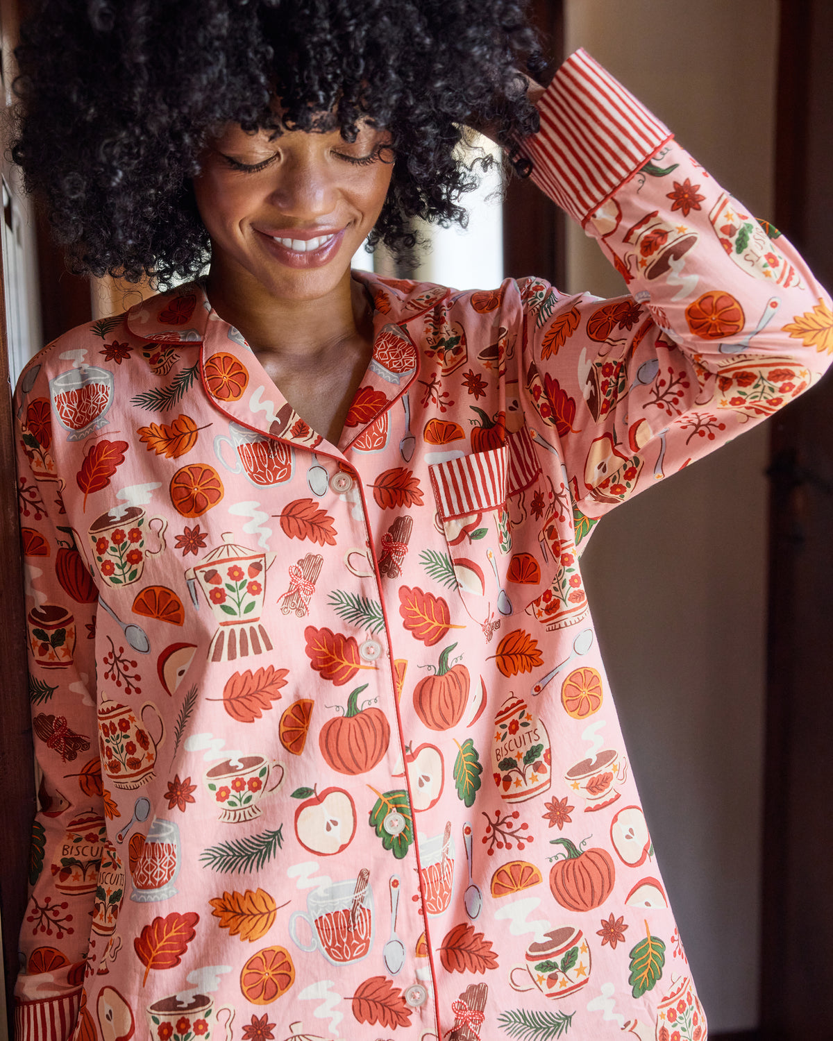 Close-up front view of the pink Autumn Cafe pajama top with notched collar, buttons, chest pocket, striped cuffs, and tea, fruit, leaf, and biscuit-jar print.