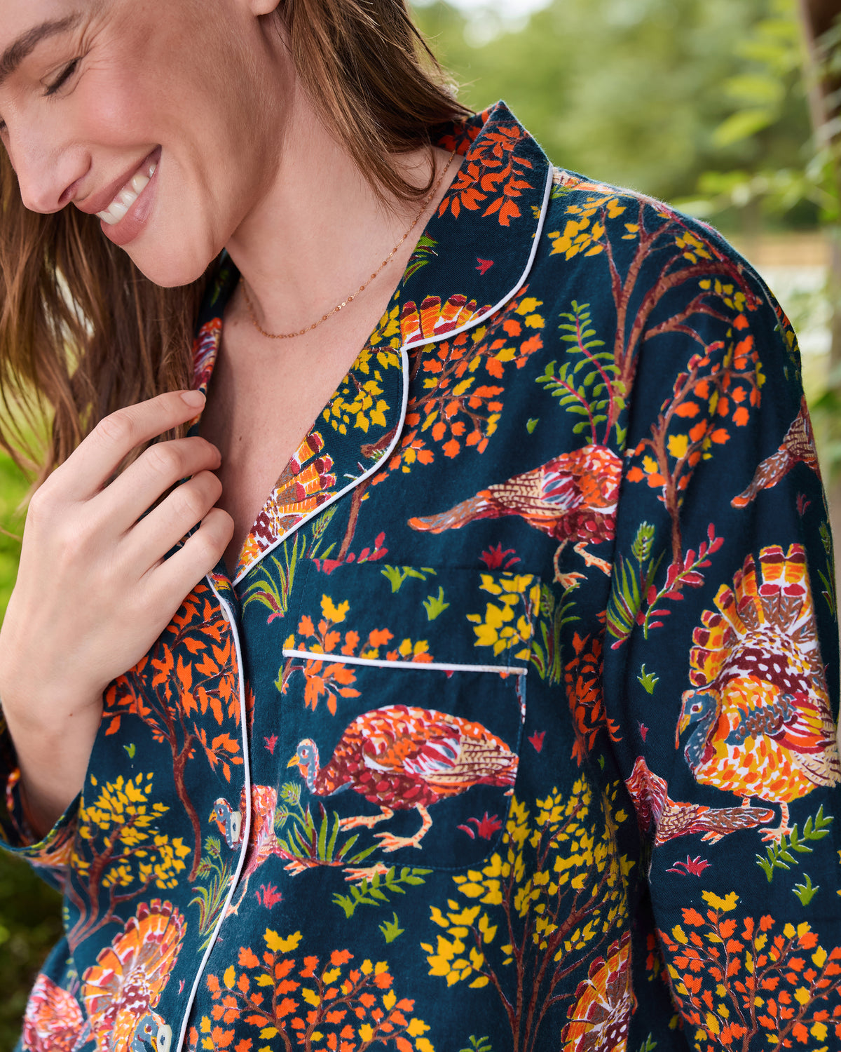 Close-up of the navy Turkey Trot pajama top showing white-piped notched collar, chest pocket, buttons, and printed turkeys among autumn foliage.