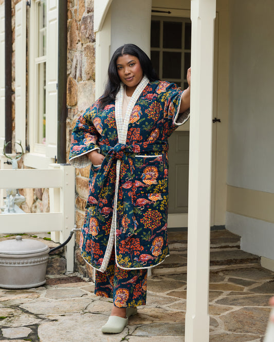 Person wearing a navy Turkey Trot quilted robe with turkey and autumn foliage print, belt, and pockets.