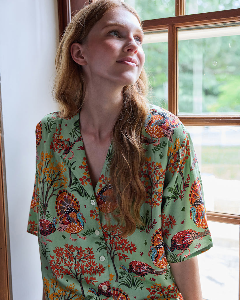 Close view of a sage short-sleeved pajama top with buttons and a colorful turkey and autumn foliage print.