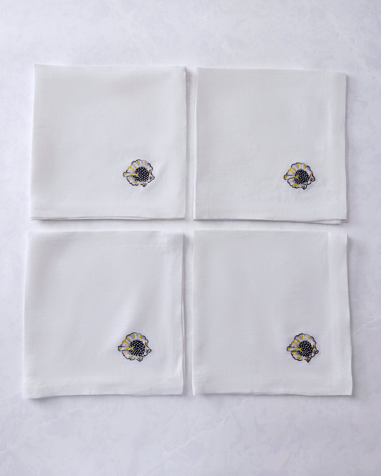 Four white dinner napkins arranged in a square, each embroidered with a shell motif.