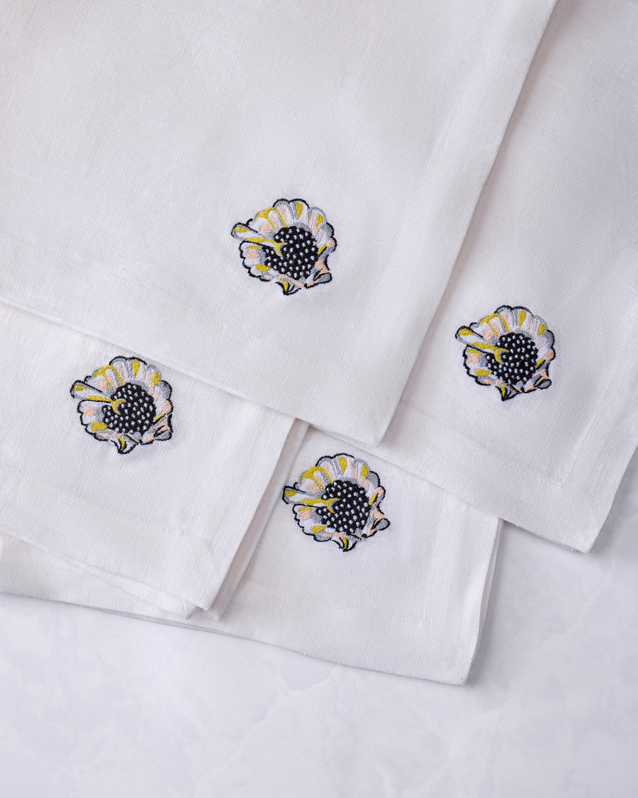 Four overlapping white dinner napkins with embroidered shell motifs.