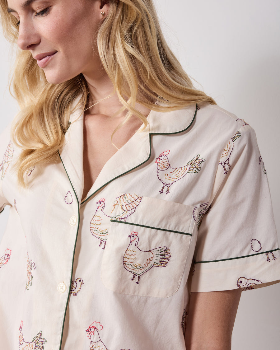 Close view of the short-sleeve pajama top showing the piped collar, chest pocket, buttons, and embroidered hen pattern.