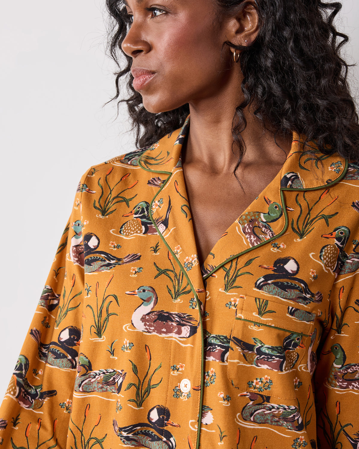 Close-up of the mustard Duck Pond long pajama top showing the notched collar, green piping, chest pocket, buttons, and duck print.
