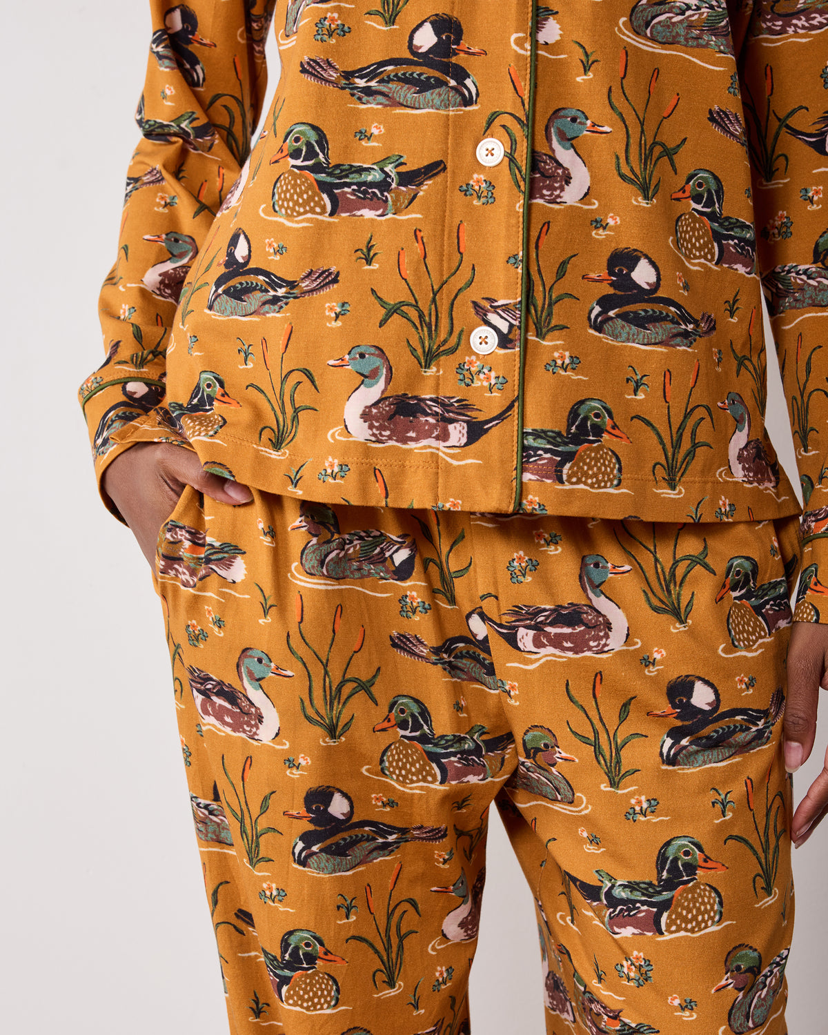 Close-up of the mustard Duck Pond long pajama set showing the buttoned top hem, piping, duck print, and pants waistband.