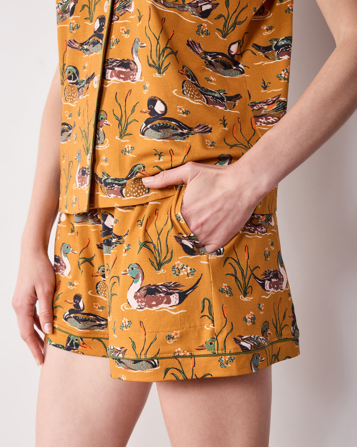 Close-up of the mustard Duck Pond short pajama set showing the printed top hem, matching shorts, and side pocket.