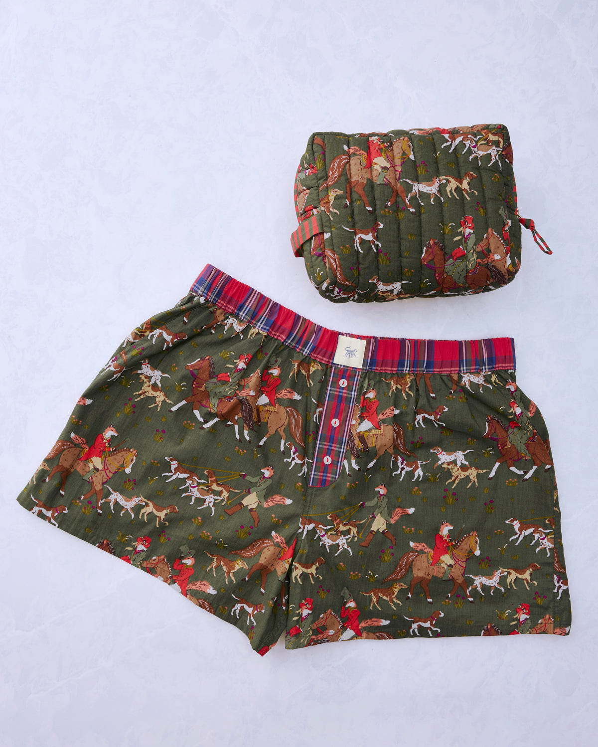 Pine-green printed pajama boxers with foxes and hounds beside a matching quilted pouch.