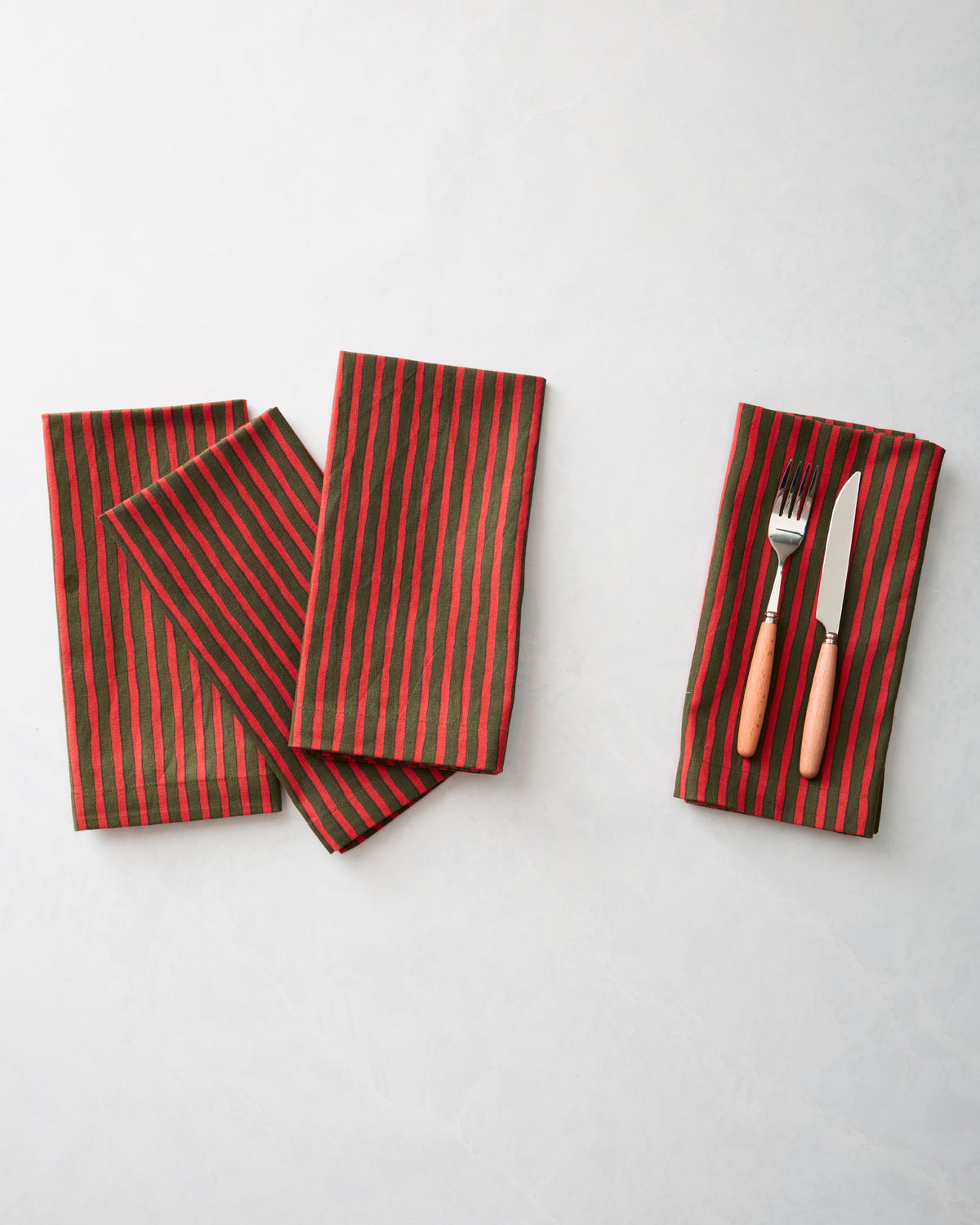 Four red-and-green striped dinner napkins, with one folded around a fork and knife.