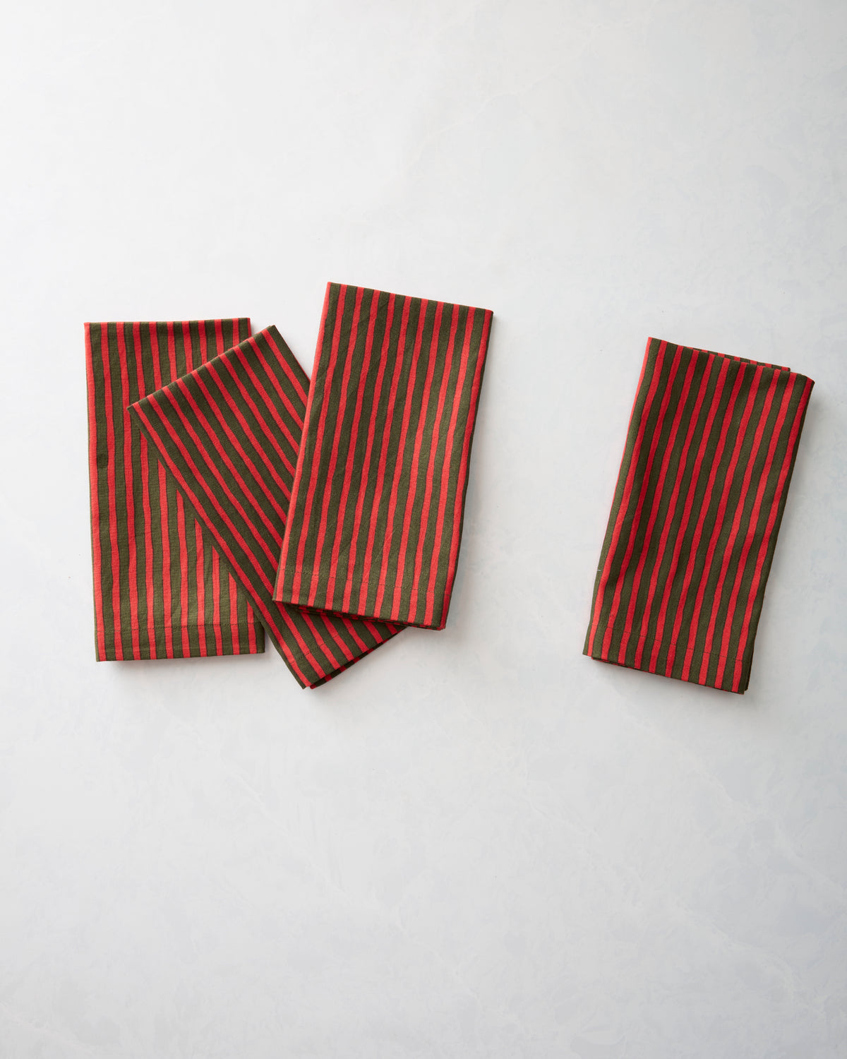 Four folded red-and-green striped dinner napkins arranged on a light background.