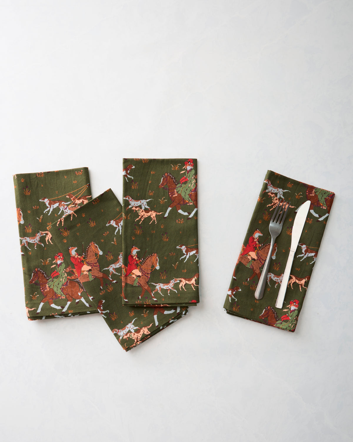 Four folded Fox & Hounds dinner napkins arranged together, with a fork and knife placed on one napkin.