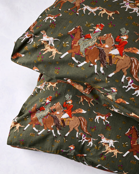 Close-up of green pillowcase fabric printed with foxes, hounds, and riders on horseback.