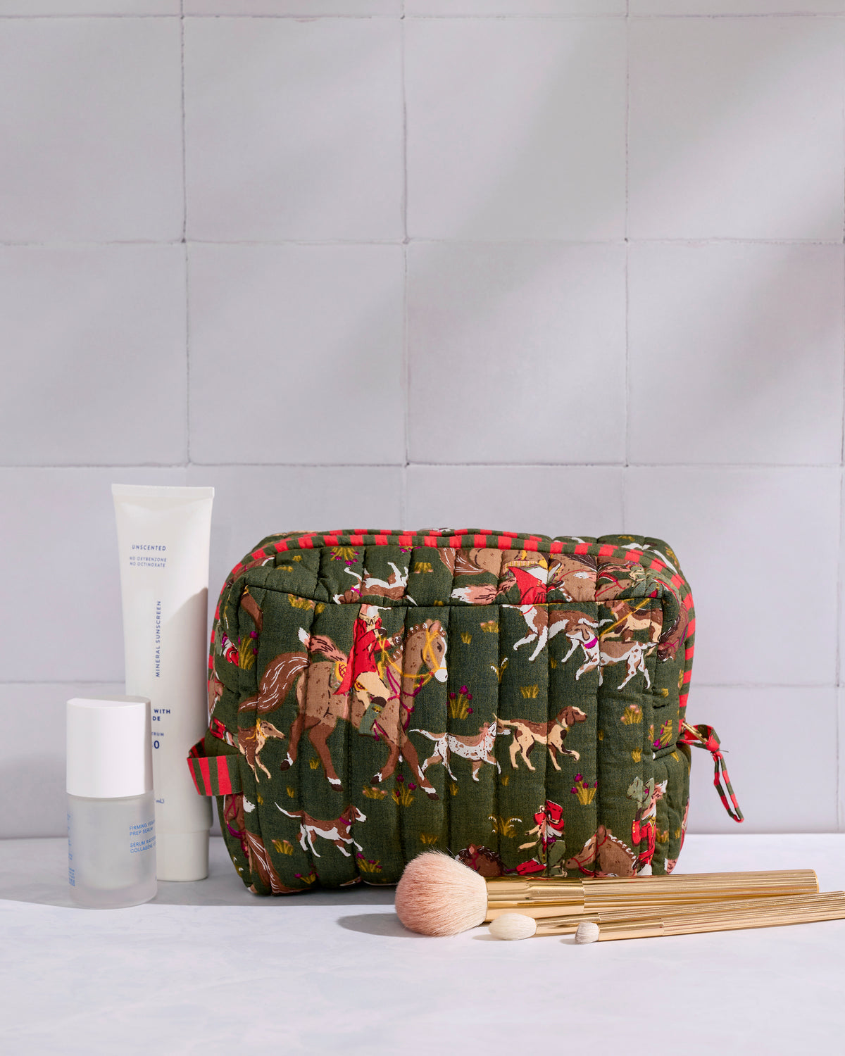 Pine Grove quilted pouch displayed with cosmetics and makeup brushes, showing its fox-and-hounds print.