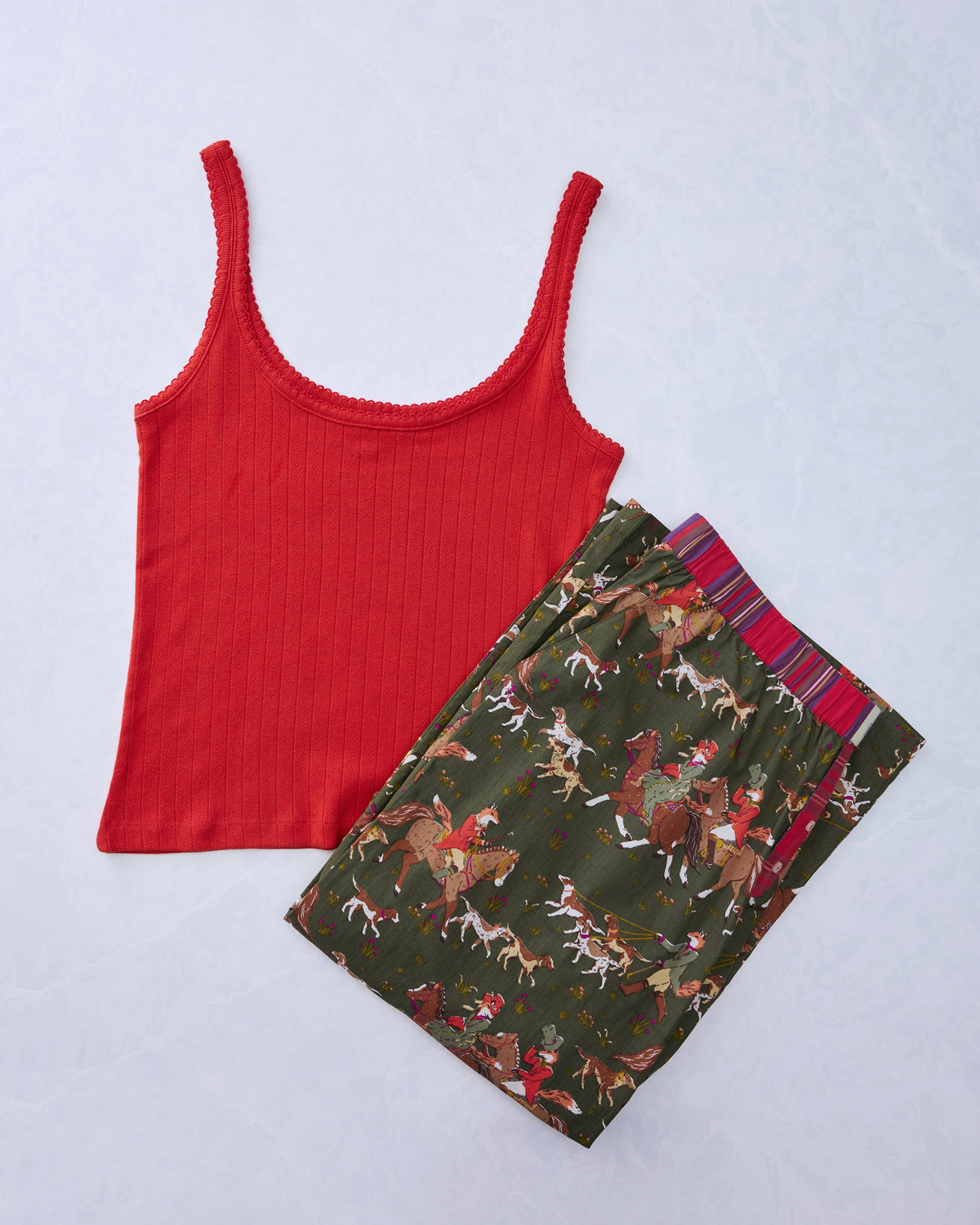 Red ribbed tank top beside pine-green pajama pants printed with foxes on horseback and hounds.