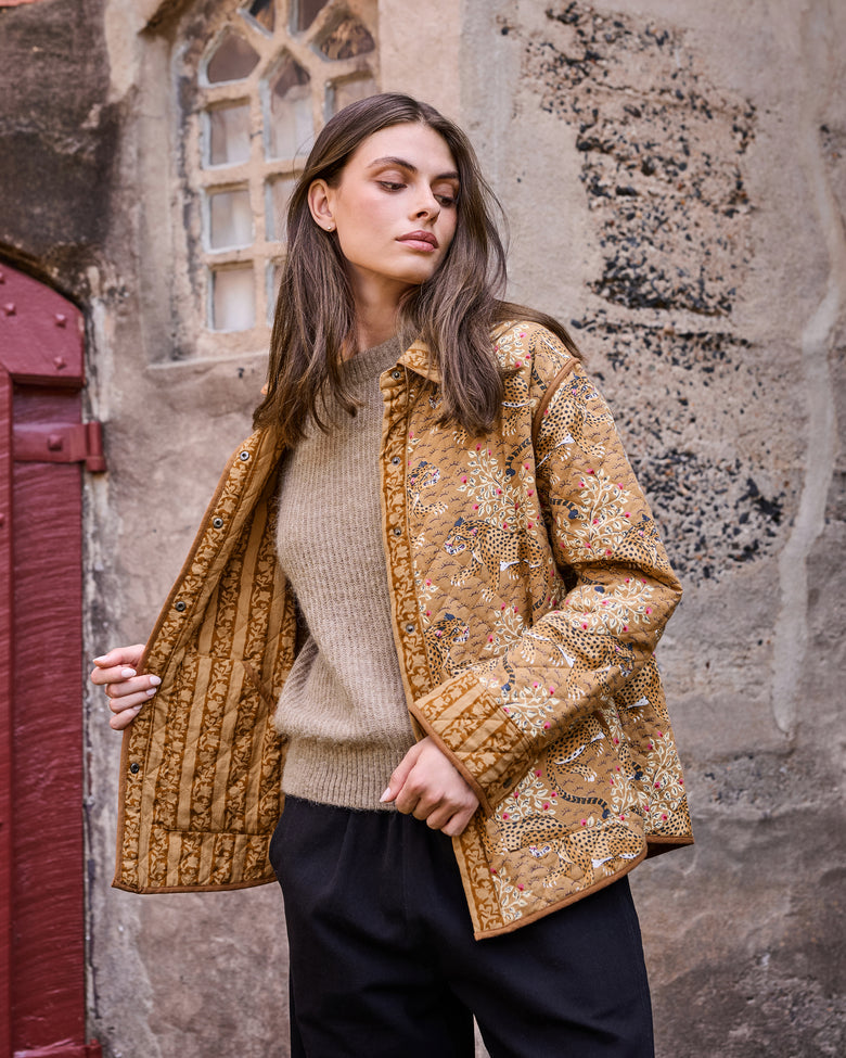 Model wearing the mustard quilted jacket open to show its contrasting botanical print lining.